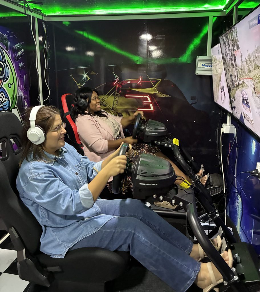 On-site corporate team building Sydney: Participants smiling while using mobile racing simulator cockpits inside a customized trailer.